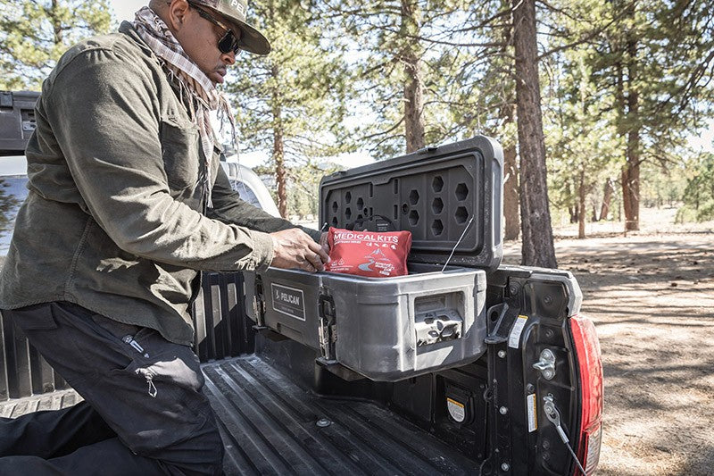 Load image into Gallery viewer, A man is putting medical kits into a black Pelican BX55S case. The BX55S is attached to the interior side of a truck bed. The truck is in the forest.
