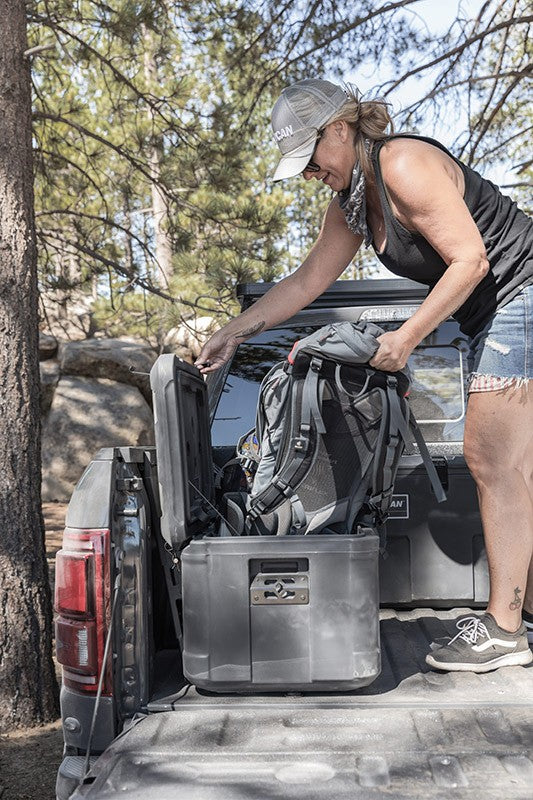 Load image into Gallery viewer, A women placing a backpack in gray Pelican Cargo BX80 case on top of a truck bed. 
